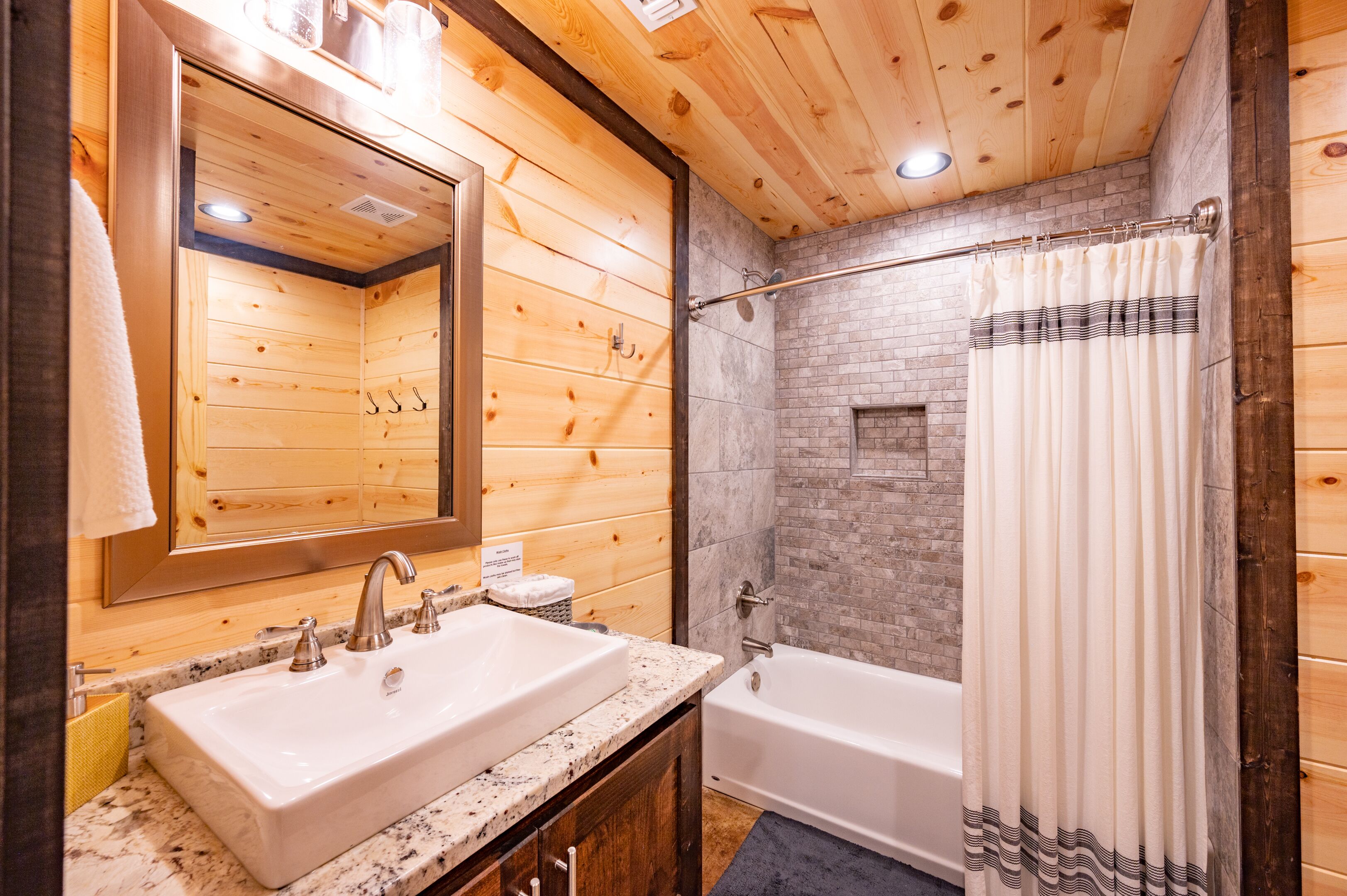 A wooden cabin bathroom with a large mirror, a sink, a bathtub, and a shower curtain.