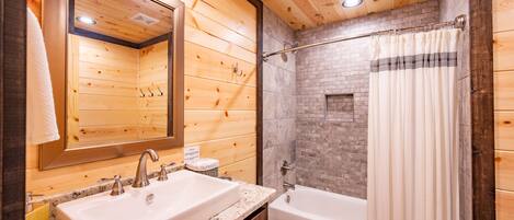 A wooden cabin bathroom with a large mirror, a sink, a bathtub, and a shower curtain.