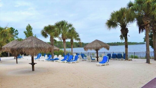 Een strand met rieten parasols en blauwe ligstoelen.