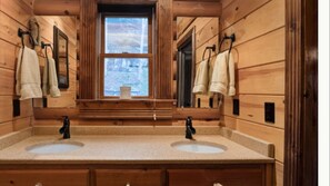 Un baño de cabaña de madera con dos lavamanos, una ventana y toallas colgadas en ganchos.