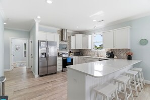 A modern kitchen with white cabinetry, stainless steel appliances, a central island with bar stools, and a herringbone-patterned backsplash.