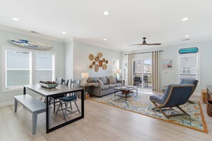 A modern living room with a dining table, sofa, and armchair, a ceiling fan, and a 'STAY SALTY' sign.