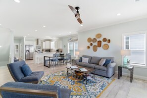 A spacious living area with a sofa, coffee table, and a dining area with chairs and a kitchen in the background.