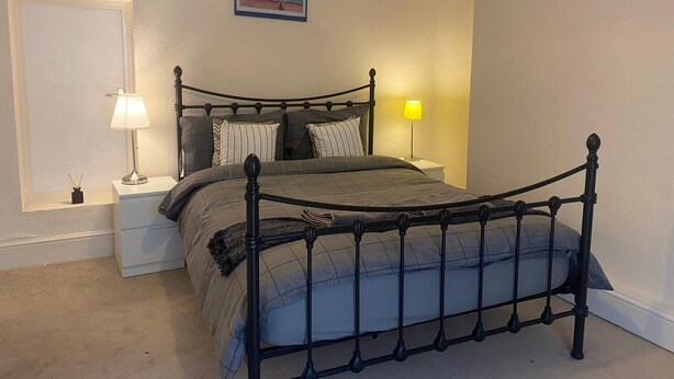 A bedroom with a bed, nightstands, lamps, and framed pictures on the walls. - Cute Convenient and close to the beech. (Brighton)