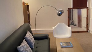 A living room with a black sofa, a white chair, a wooden coffee table, and a floor lamp. - Cute Convenient and close to the beech. (Brighton)
