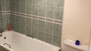 A bathroom with a bathtub, green tiles, a toilet, and a small framed picture on the wall. - Cute Convenient and close to the beech. (Brighton)