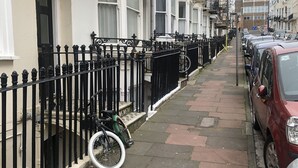 A row of terraced houses with black metal fences, a bicycle, and parked cars on a paved street. - Cute Convenient and close to the beech. (Brighton)