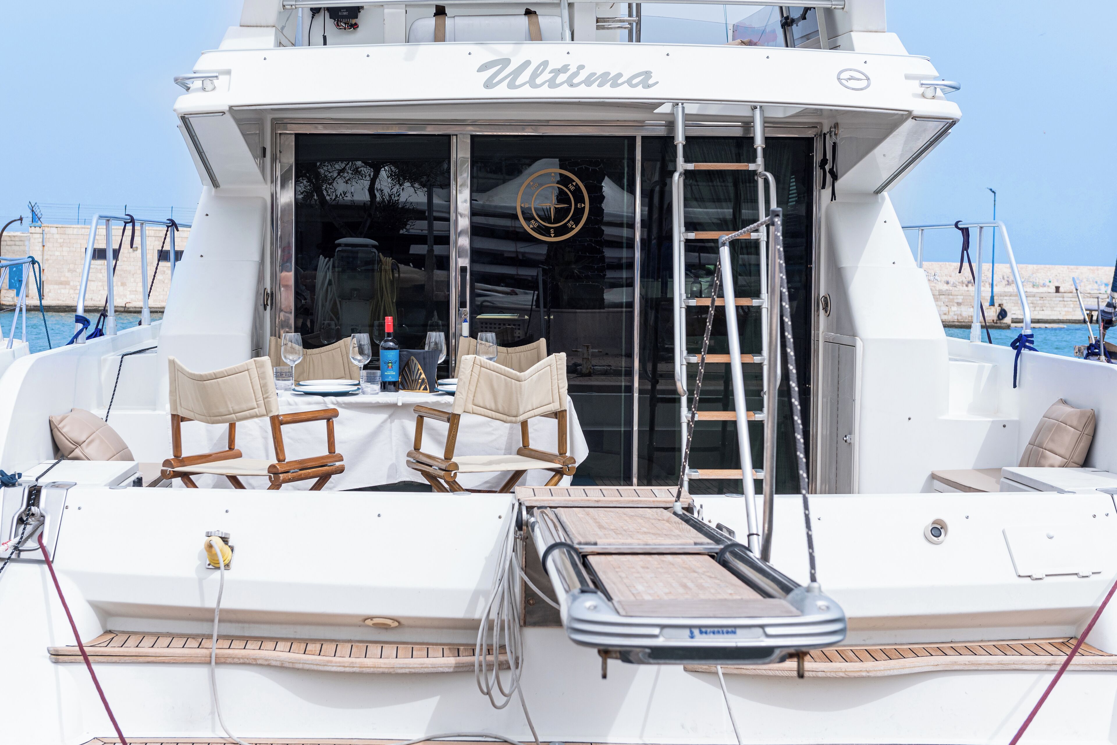 Eine Yacht namens 'Ultima' mit überdectem Deck, Liegestühlen und einem kleinen Tisch mit Flasche und Glas.
