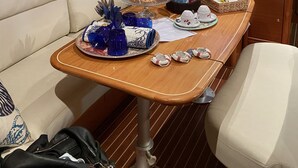 A cozy cabin interior with a wooden table set for breakfast, a television displaying a scenic landscape, and a cushioned seating area. - Gi&Gi ULTIMA......... a boat for dreaming (Bari)