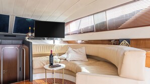 A boat interior with a wooden deck, a sofa, a small table with a bottle and glass, and a flat-screen TV mounted above the sofa. - Gi&Gi ULTIMA......... a boat for dreaming (Bari)