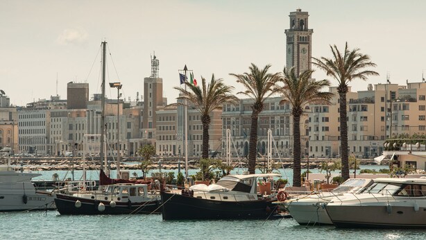 A marina with several boats docked, a prominent tower in the background, and a row of palm trees. - Gi&Gi ULTIMA......... a boat for dreaming (Bari)