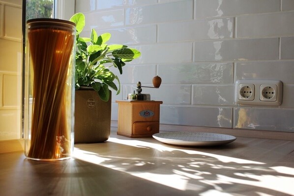 A kitchen with a tall glass vase, a potted plant, a wooden spice rack, and a plate on the counter.