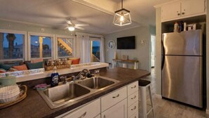Una cocina moderna con refrigerador de acero inoxidable, lavamanos doble y una zona de comedor con taburete de bar.
