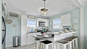 Una cocina moderna con armarios blancos, una isla central con taburetes altos y una lámpara colgante.