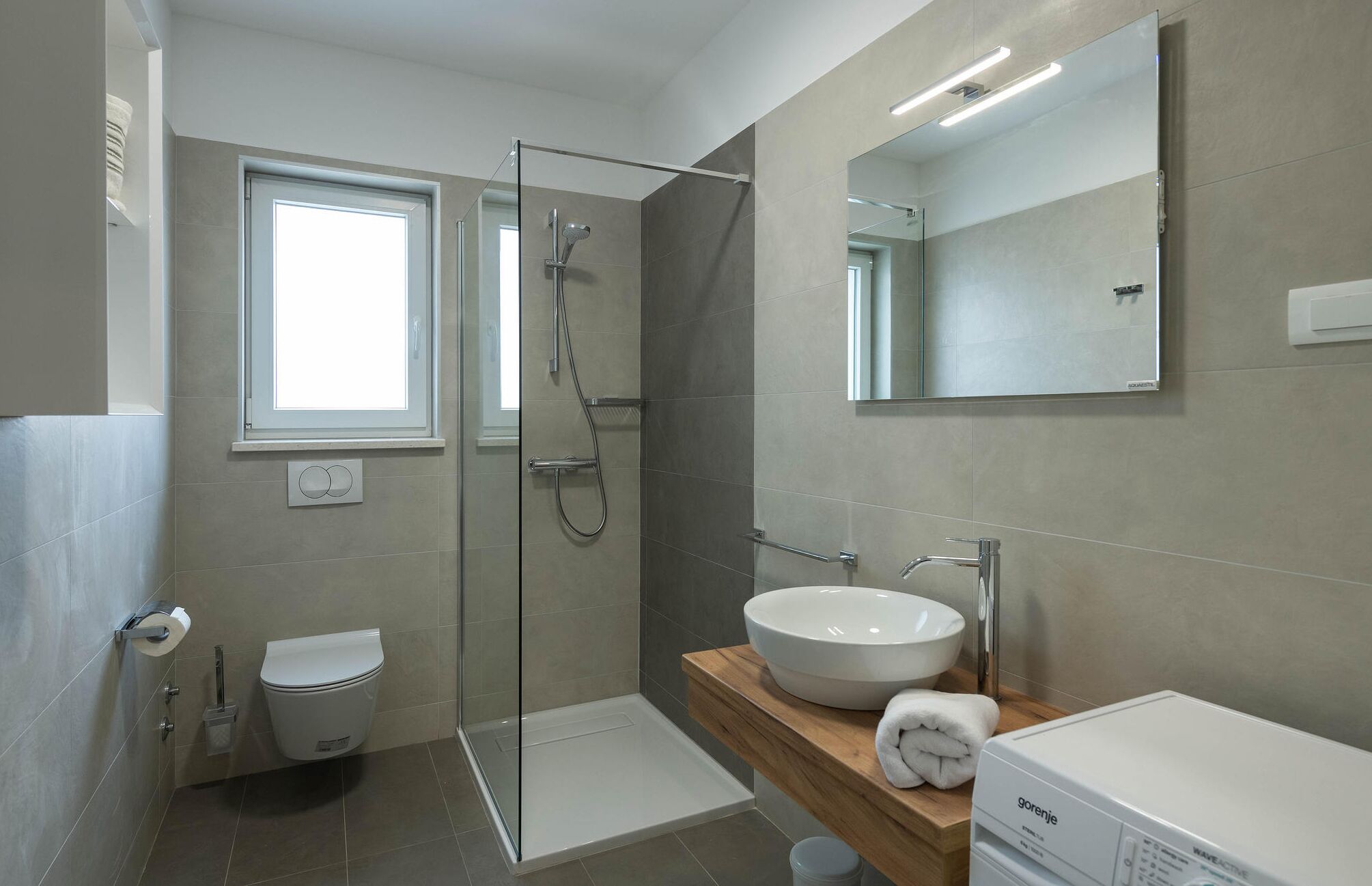 A modern bathroom with a glass-enclosed shower, a white toilet, and a sink with a wooden countertop.