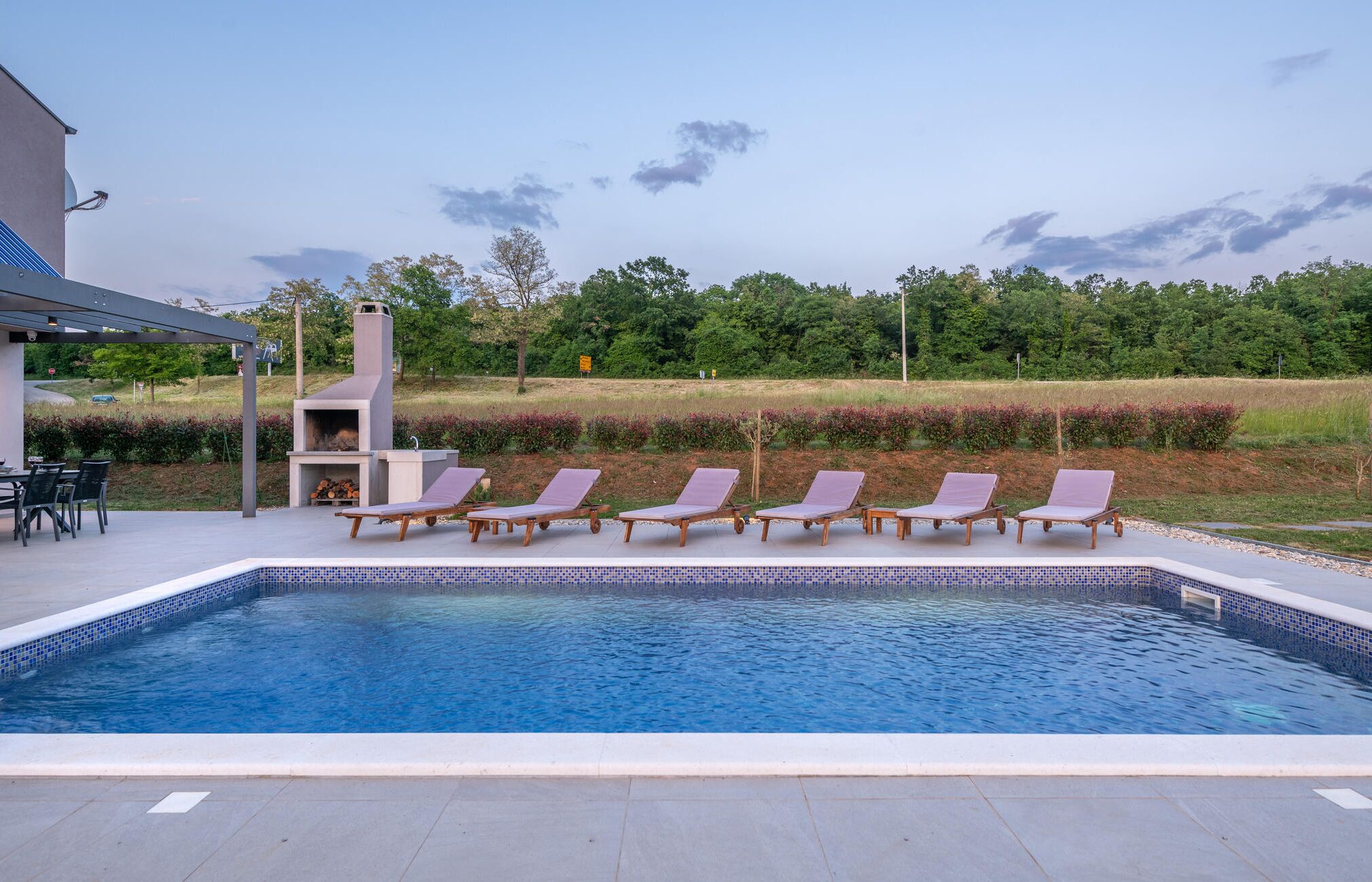 Une piscine avec des chaises longues et un espace barbecue.