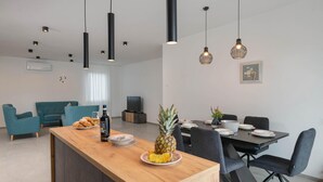 Een moderne woonkamer met een houten kookeiland, een eethoek met tafel en stoelen, en een keuken met een fornuis.