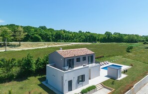 Ein modernes, zweistöckiges Haus mit Swimmingpool, umgeben von einer üppigen grünen Landschaft.