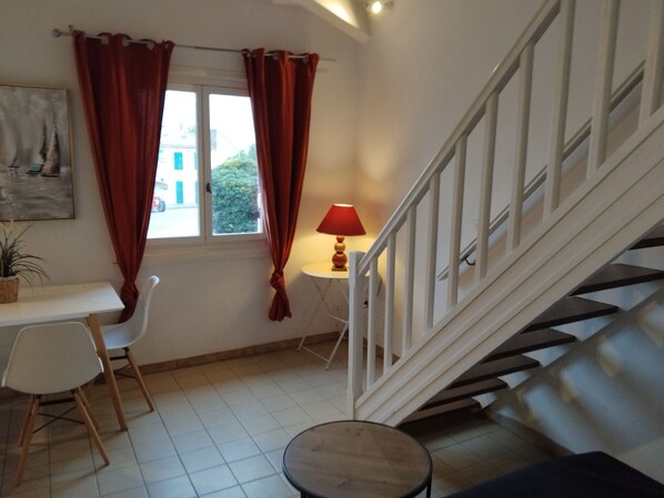 A room with a staircase, a dining table with chairs, a small table with a lamp, and a potted plant. - Renovated, town center, dishwasher, air-conditioned, WIFI, TV , double glazing (Saintes-Maries-de-la-Mer)
