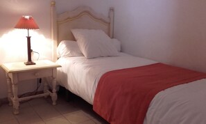 A single bed with white bedding and a red blanket, a bedside table with a lamp, and a plain wall. - Renovated, town center, dishwasher, air-conditioned, WIFI, TV , double glazing (Saintes-Maries-de-la-Mer)