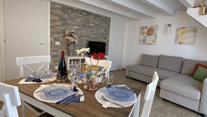 A dining area with a wooden table set for a meal, white chairs, a fireplace, and a staircase.