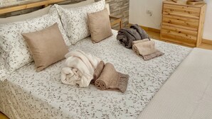 A bedroom with a stone-patterned headboard, a wooden dresser with a mirror, and a bed with floral bedding and rolled towels.