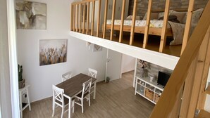 A loft-style bedroom with a wooden bunk bed, a dining area with a table and chairs, and a staircase leading to an upper level.