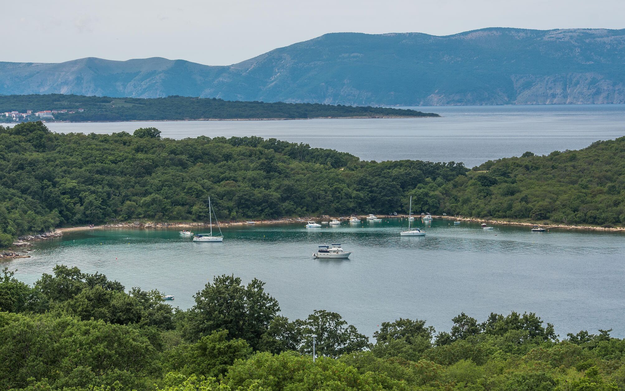 A coastal area with boats on the water, surrounded by dense green hills.