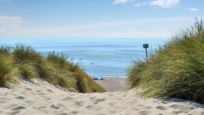 Un sentier de sable qui longe la plage et mène à la mer, avec un panneau indiquant un itinéraire côtier.