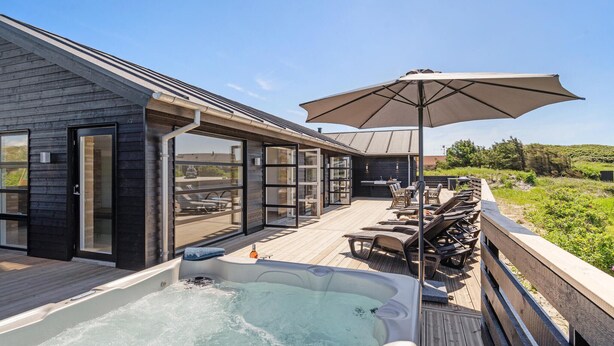 Une terrasse extérieure moderne dotée d’un jacuzzi, de chaises longues et d’un espace salon couvert avec un parasol.