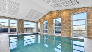 Une piscine intérieure moderne, dotée de grandes fenêtres et d’un mur en briques.