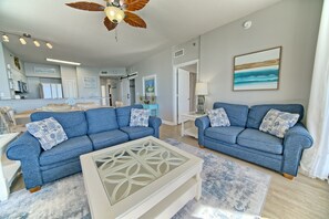 A modern living room with two blue sofas, a white coffee table, and a ceiling fan.