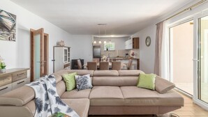 A modern living room with a beige sectional sofa, a dining area, and a kitchen in the background. - Beautiful home in Orihi (Orihi)
