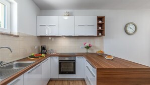A modern kitchen with white cabinets, a built-in oven, a wooden countertop, and a clock on the wall. - Beautiful home in Orihi (Orihi)