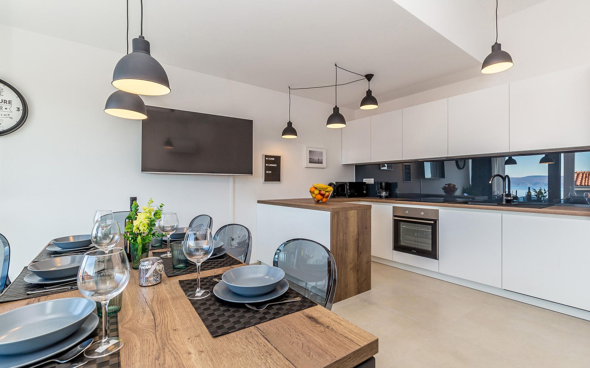 A modern kitchen with white cabinets, a wooden countertop, and black pendant lights.
