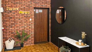 A room with a brick wall, a wooden door, a mirror, a table with a vase, and a potted plant. - 4 bedroom lovely home in Zalewo (Zalewo)