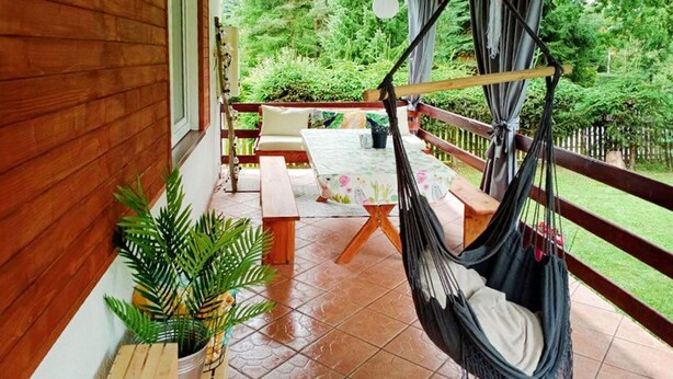 A wooden balcony with a hammock, a table with a floral tablecloth, and a potted plant. - 4 bedroom lovely home in Zalewo (Zalewo)