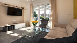 A modern living room with a flat-screen TV, a glass coffee table, a sofa, and a chair.
