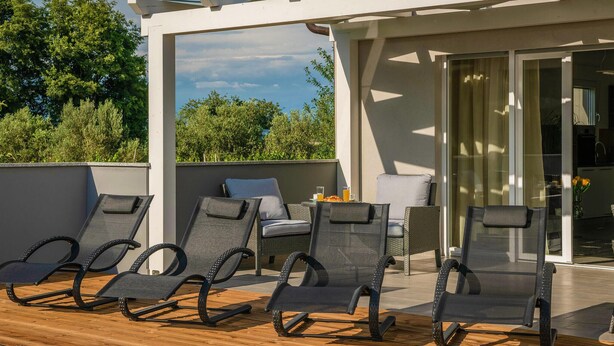 A rooftop terrace with four lounge chairs, a small table, and a glass door leading to a kitchen area.