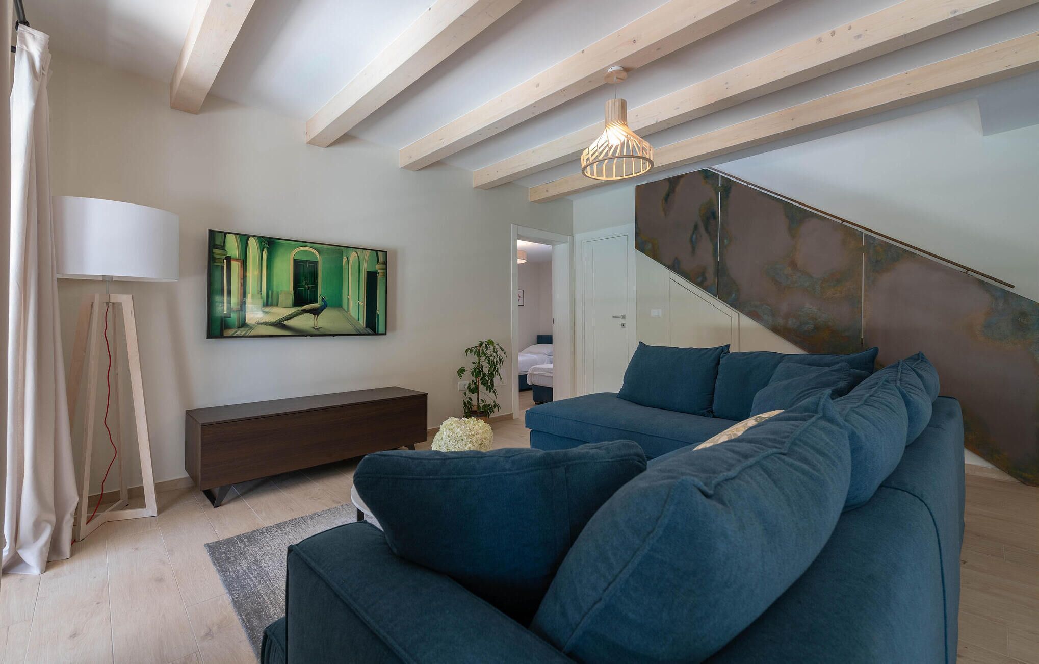 Ein modernes Wohnzimmer mit einem blauen Sofa, einem Flachbildfernseher und einer Wendeltreppe mit Metallwand.
