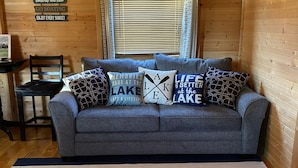 A cozy cabin interior with a grey sofa, striped rug, and lake-themed pillows. - Cozy Cabin with private back yard, located 5 min away from Dale Hollow Lake (Albany)