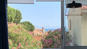 A window with a view of a coastal town, including buildings and a clear sky. - Appartement 4 personnes vue mer (Collioure)