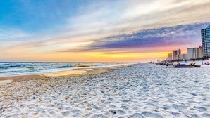 Een strand bij zonsondergang, met een zandstrand en gebouwen op de achtergrond.
