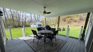 A covered outdoor deck with a table and chairs, a ceiling fan, and a view of a grassy yard. - CHARMING HOME CLOSE TO WATKINS GLEN & INTERNATIONAL RACETRACK (Montour Falls)