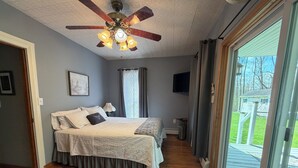 A bedroom with a ceiling fan, a bed with a white bedspread, a window with curtains, and a view of the outdoors. - CHARMING HOME CLOSE TO WATKINS GLEN & INTERNATIONAL RACETRACK (Montour Falls)