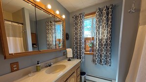 A bathroom with a large mirror, a sink, wooden cabinets, a window with patterned curtains, and a towel rack. - CHARMING HOME CLOSE TO WATKINS GLEN & INTERNATIONAL RACETRACK (Montour Falls)