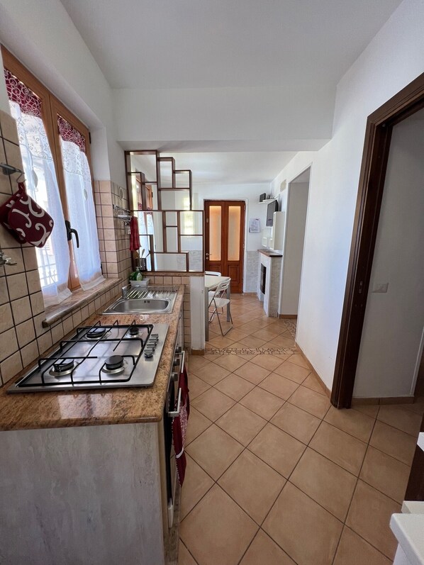 A modern kitchen with a gas stove, a sink, and a dining area with a chair. - Villa Bebe' : Splendida Casa Vacanze in Costiera Sorrentina!!!! (Vico Equense)