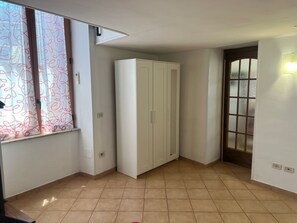 A room with a tiled floor, a white wardrobe, a window with patterned curtains, and a door with frosted glass panels.