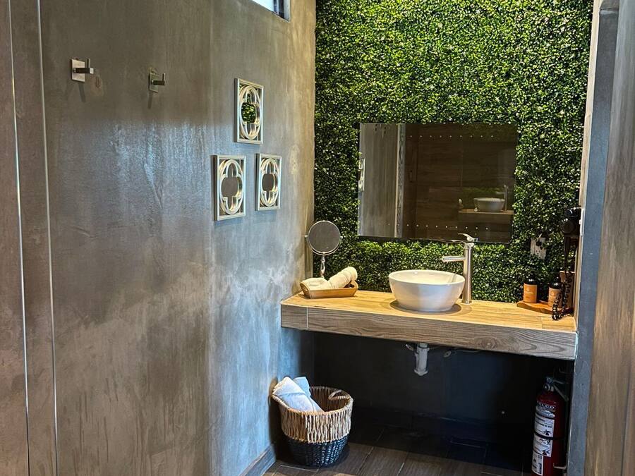 Un baño moderno con una pared cubierta de hojas verdes, un tocador de madera, un lavamanos blanco y un inodoro.