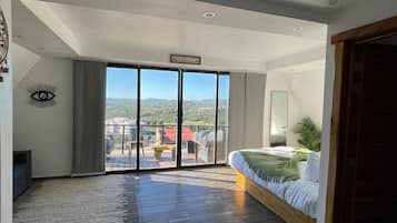 A spacious room with a large sliding glass door leading to a balcony, a bed with a green throw, and a wooden bench.